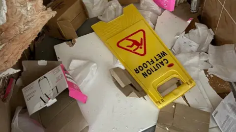 Daniel Berkoh-Gyamfi A caution for wet floor sign amongst paper all over the floor and other rubbish. 