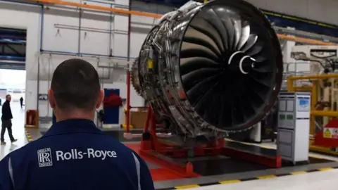 Getty Images A Rolls-Royce worker looks on at a huge jet engine inside a factory