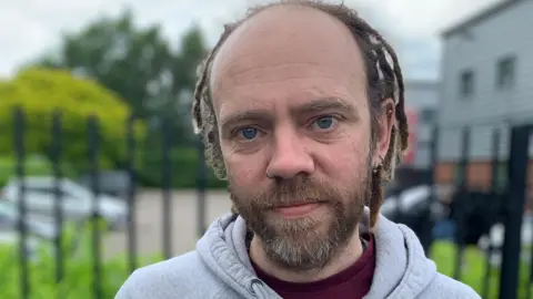 BBC A man with dreadlocks and piercings standing outside a house