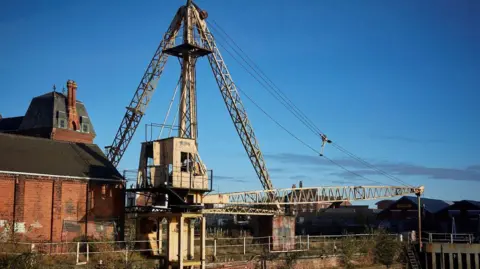 Hull Maritime The crane in its original position. The main jib of the crane is hovering over the River Hull. The colour of the crane is beige, rather than the bright yellow that it has been painted into. 