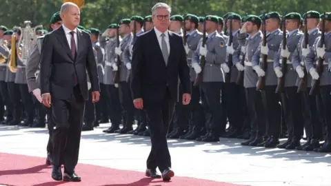 Getty Images German Chancellor Olaf Scholz and UK Prime Minister Sir Keir Starmer walk down a red carpet outside Chancellery in Berlin, in front of a military guard of honour