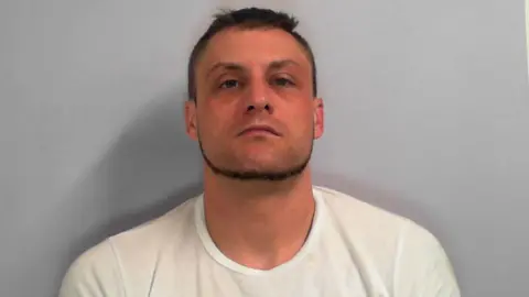 North Yorkshire Council Custody picture of a man with short hair and a short beard, wearing a white t-shirt.