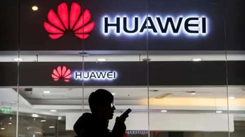 Getty Images A pedestrian talks on the phone while walking past a Huawei store in Beijing