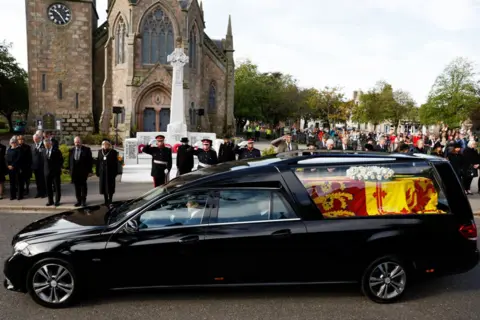 Jeff J Mitchell/Getty Images People line the street as the hearse carrying the coffin passes through the village of Ballater, near Balmoral