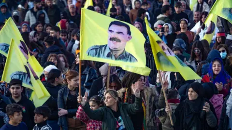 A crowd of people, some holding yellow flags bearing pictures of PKK founder Abdullah Ocalan