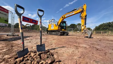 Dos palas clavadas en el suelo cerca del cruce de Kirk Hill, con una excavadora al fondo.