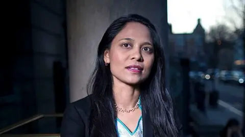 Rushanara Ali stares into the camera against a city street background.