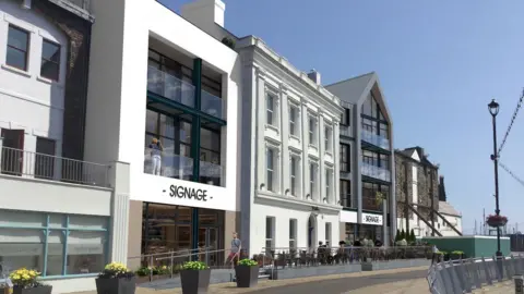 Two modern buildings with large windows and balconies are on either side of a grand white Victorian building on the quay, there is scaffolding still in place on the derelict building on the right of the development.