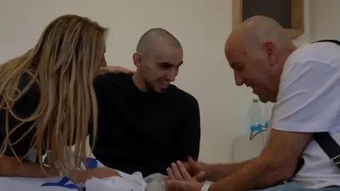 Reuters Rom Braslabski, with close-cropped hair and a black T-shirt smiles as he chats to a man in a white T-shirt and a woman with long blonde hair
