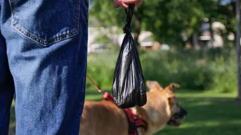 Getty Images Dog poo bag and a man holding it with a dog in the background