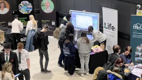 A shot of a hall, taken from above, looking down on several stalls of employers such as Life 2020 and lots of students milling around