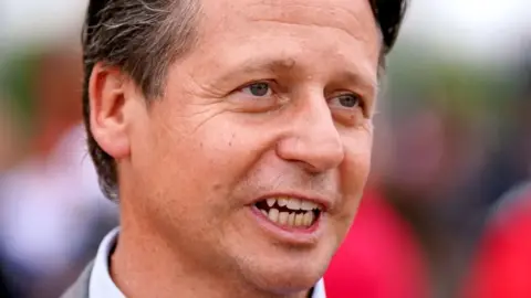 A man with brown hair against a multicoloured background