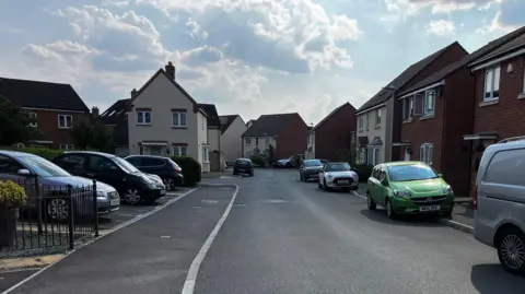 Attlebridge Way in Gloucestershire. It is a residential street with houses and cars on both sides of the road.
