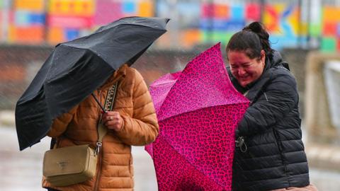 Two women struggle with umbrellas in the rain in Liverpool