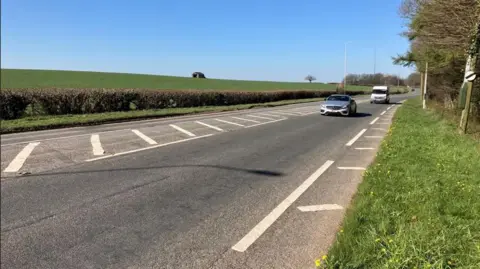 BBC The A48 near Bonvilston in the Vale of Glamorgan. A single lane with a car and a van travelling along it. A national speed limit sign is visible. 