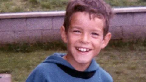 An archive photo of the late Shaun McLaughlin.  The schoolboy has short, dark hair and a broad smile.  He is wearing a blue hooded top with a black collar. 