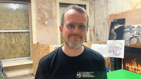 Photograph of Ed Bailey from the Lancashire Wildlife Trust. He is pictured in a room at Rock Hall with boarded-up windows in the background.