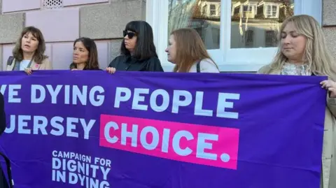 Five women hold up a purple sign by the Campaign for Dignity in Dying