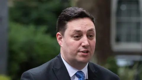 Getty Images Lord Houchen. He has short, dark hair and is clean shaven. He is wearing a dark suit, white shirt and light blue tie.