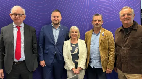 Five candidates, four men and one woman, stand in front of a purple BBC radio studio background.