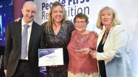 Nottingham University Hospitals NHS Trust Four people, Margaret Wildgust, among them, at an awards ceremony where she is being presented with the volunteering award and certificate