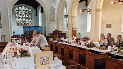 The nativity scenes are on display in the church on white tables laid out over church pews.