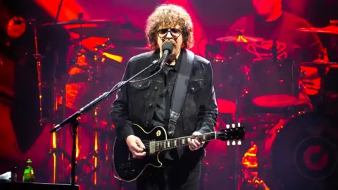 Jeff Lynne performs on stage with a guitar