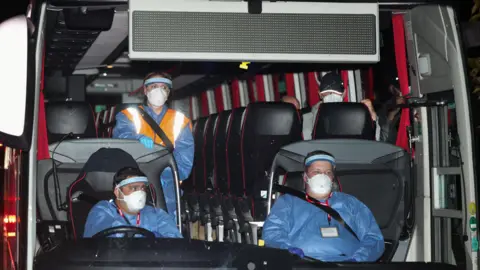 Reuters Three people wear protective overalls and face coverings on a bus transporting repatriated British nationals to Arrowe Park Hospital in Merseyside 