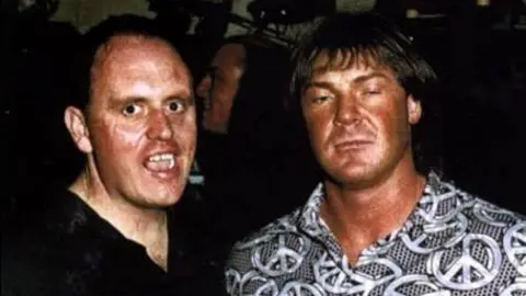 Bernard O'Mahoney Bernard O'Mahoney is wearing a black shirt and has his mouth open. He is next to Tony Tucker, who is wearing a black and silver shirt with peace symbols on it.