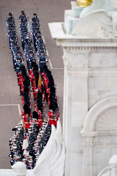 PA Media A narrow aerial view shows various groups of military parading down the Mall with the statue in front of Buckingham Palace in the foreground.
