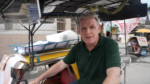 Jonathan Head sits on a bike as he speaks to the camera in the Philippines
