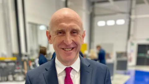 A man in a suit and tie in a factory smiling at the camera