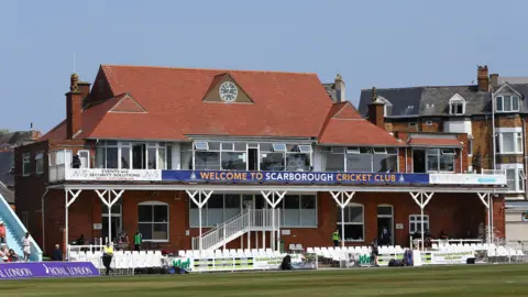 Getty Images A cricket pavilion, pictured from a cricket pitch. The words 'Welcome to Scarborough Cricket Club' are emblazoned across the pavilion. Empty seats are seen at the foot of the pavilion.
