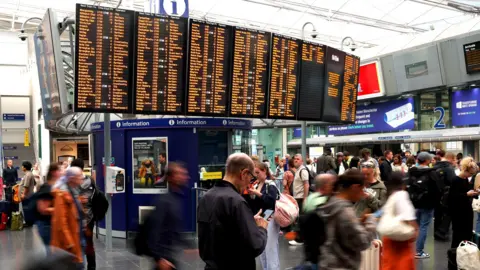 Getty Images Passengers walk in front a screen showing information about cancellations inside Manchester Piccadilly train station after a major disruption to rail service in the Midlands and northwest England on August 06, 2026 in Manchester, England. 