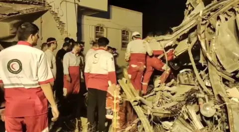  EPA-EFE A screen grab shows members of the Iranian Red Crescent Society inspecting a pile of wreckage at the bus crash site. 