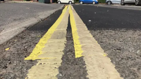 BBC/Seb Cheer Two sets of double yellow lines painted on the same stretch of road, overlapping. In this image, one of the sets of lines stops but the other continues.