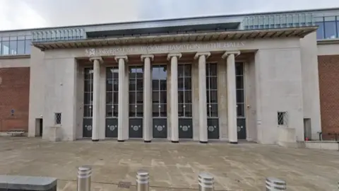 A large grey stone and brick building with pillars in the centre. University of Wolverhampton at The Halls is written above the entrance.