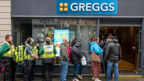 Customers queuing outside of Greggs on a rainy day