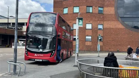 A red double decker bus in a town centre. 