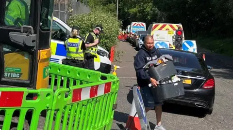 A man holding a two baskets of goods leaves a street that has police officers guarding