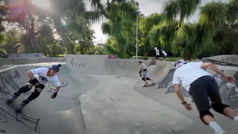 Two men on skateboards and one on roller blades at the skate park in Winchester