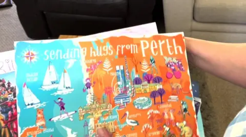 BBC Woman holding a hand-made card saying "sending hugs from Perth