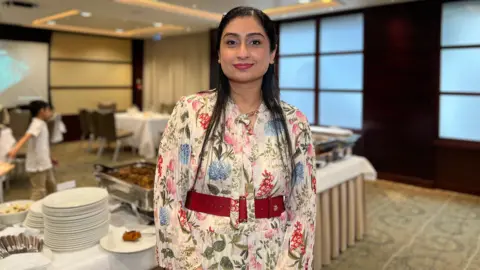 Samya Javid looks at the camera in floral dress in a tradition style standing in front of the food