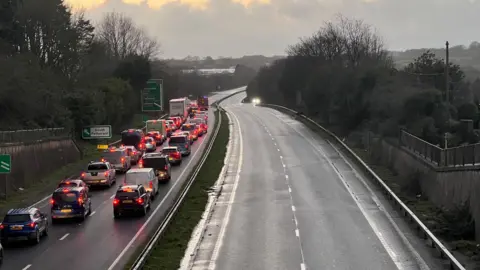 A long queue of standstill traffic on a dual carriageway. The carriageway in the opposite direction is empty.