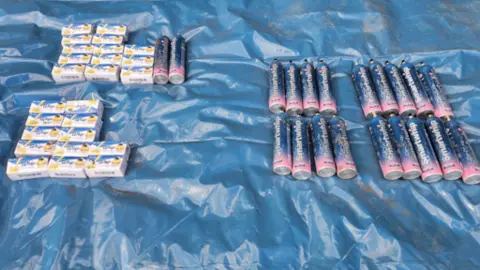 Cheshire Police Large pile of black cannisters on a blue tarpaulin in a field with a spade next to it.