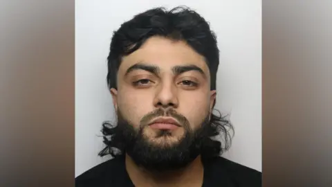 Luqman Khan, an Asian male with long black hair and a black beard.