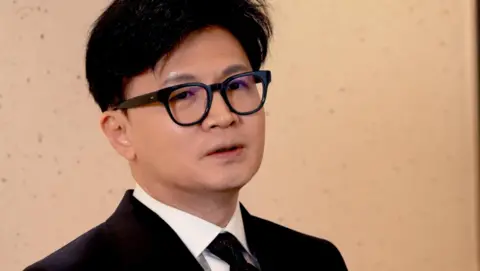 BBC News A close-up of Han Dong-Hoon, wearing glasses and a black suit