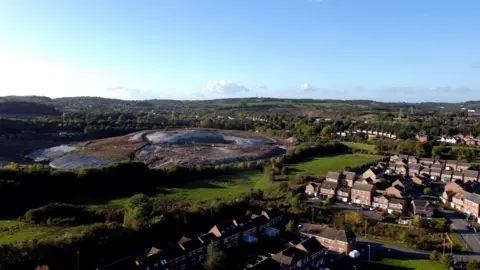 An aerial view of a landfill site, located in a field next to a village.