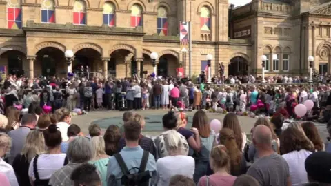 PA Media A crowd of people taking part in a vigil outside Southport's sandstone-coloured The Atkinson