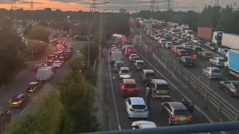 Eddy Keiller This picture taken from a bridge above a road shows three different roads, all dual-carriageway, gridlocked. Cars, vans and lorries are top to tail queuing during dusk. The queues are huge and cover the entire picture.